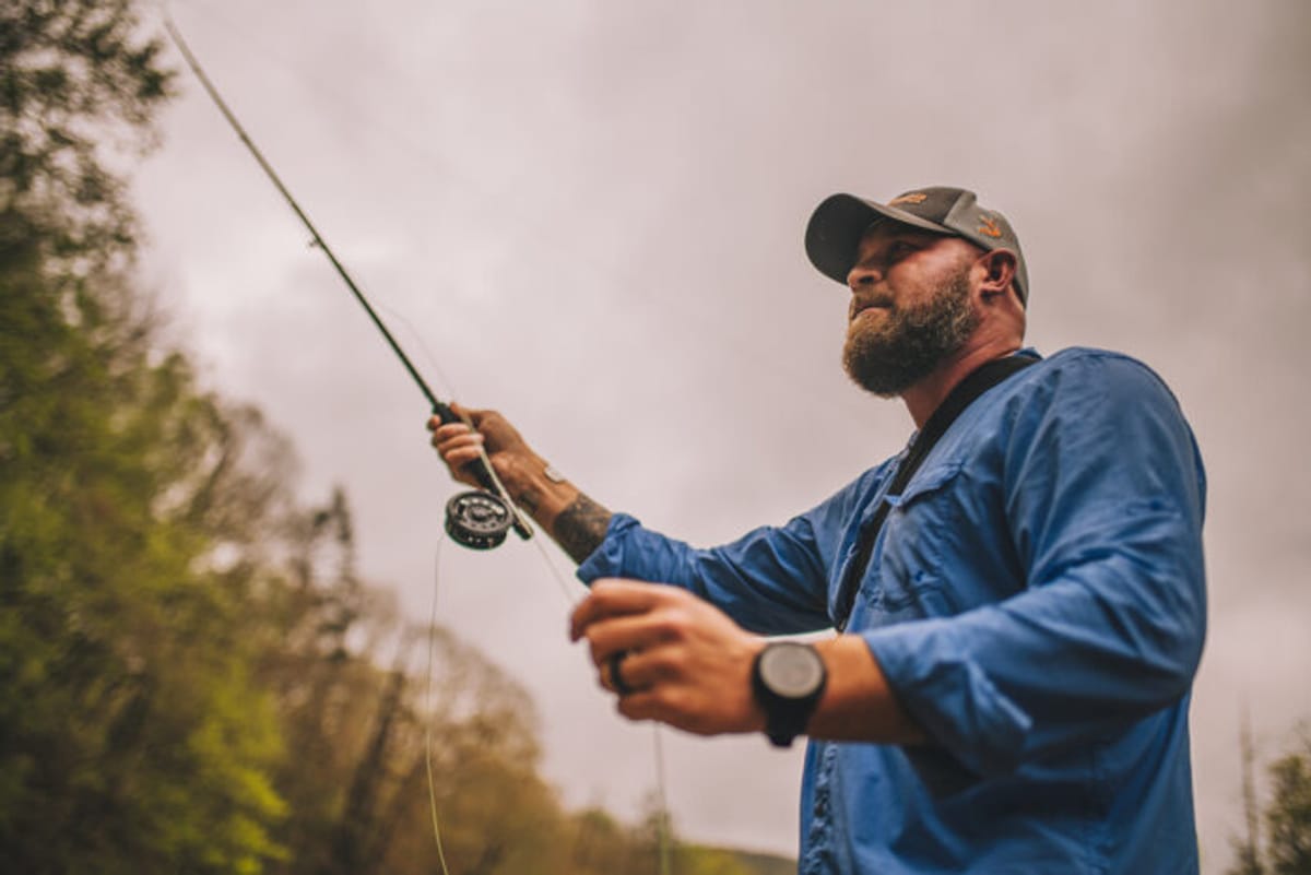 Medium shot of man casting a line in the water.